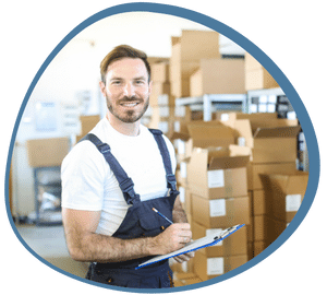 A warehouse worker with boxes in the background. He is holding a document to checking his stocks. He is using this experience to extend his canadian work permit